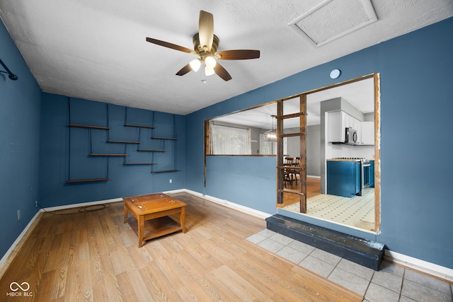 interior space featuring attic access, baseboards, a ceiling fan, and wood finished floors