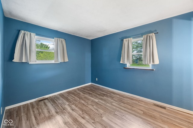 spare room featuring baseboards, visible vents, and wood finished floors