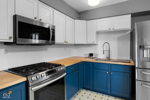 kitchen featuring wooden counters, stainless steel appliances, white cabinets, light floors, and blue cabinets