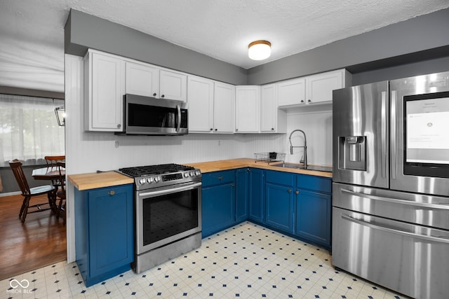 kitchen with stainless steel appliances, butcher block countertops, blue cabinets, and a sink