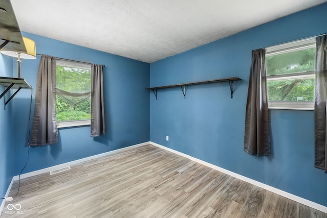 spare room with a textured ceiling, visible vents, wood finished floors, and baseboards