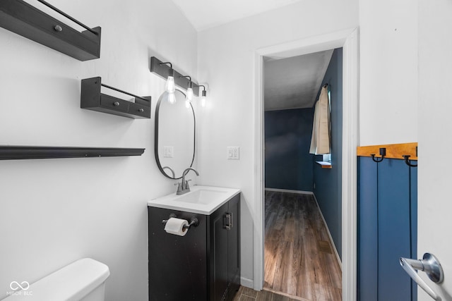 half bathroom featuring toilet, baseboards, vanity, and wood finished floors
