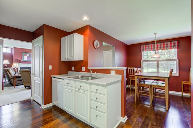 kitchen with dark wood finished floors, dishwasher, a sink, light countertops, and a peninsula