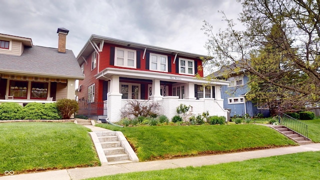 view of front facade with a porch, brick siding, a chimney, and a front yard