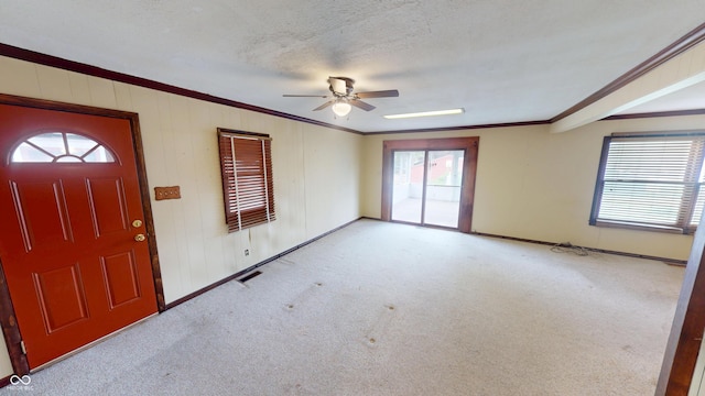 foyer entrance with crown molding, carpet, ceiling fan, and visible vents