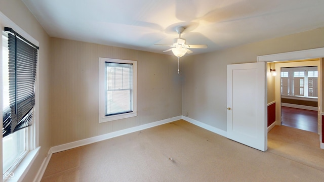 empty room with baseboards, a ceiling fan, a wealth of natural light, and light carpet
