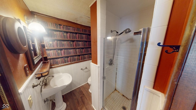 full bathroom featuring wood finished floors, wainscoting, a stall shower, and toilet