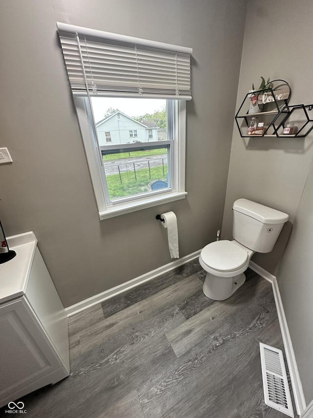 bathroom with baseboards, toilet, wood finished floors, and visible vents
