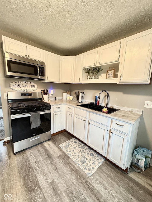 kitchen featuring open shelves, wood finished floors, a sink, stainless steel appliances, and white cabinetry