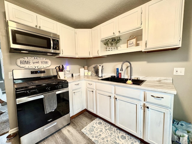 kitchen featuring white cabinets, a sink, a textured ceiling, stainless steel appliances, and wood finished floors
