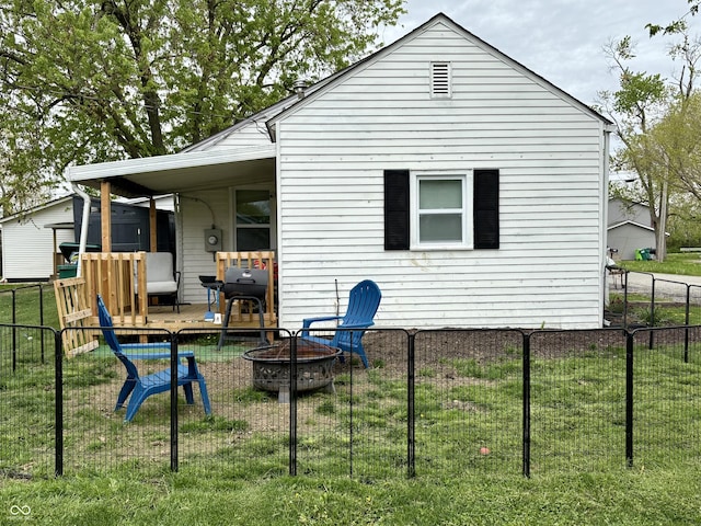 rear view of property with a lawn, fence, and an outdoor fire pit