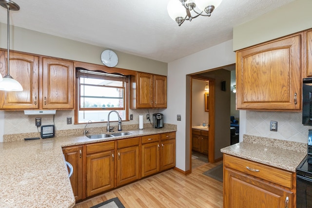 kitchen featuring a sink, light wood finished floors, brown cabinetry, tasteful backsplash, and pendant lighting