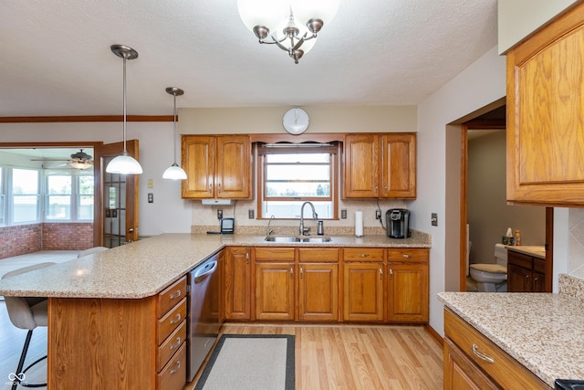 kitchen with brown cabinets, a sink, light wood-style floors, dishwasher, and a peninsula