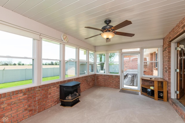 unfurnished sunroom featuring ceiling fan and a wood stove