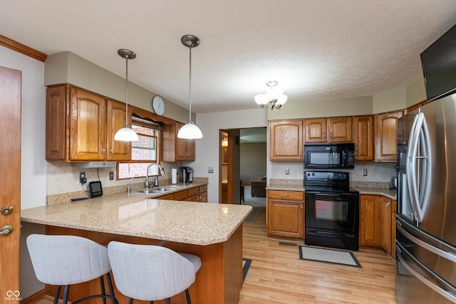 kitchen featuring a peninsula, brown cabinets, a sink, backsplash, and black appliances