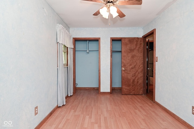 unfurnished bedroom with baseboards, a ceiling fan, multiple closets, and wood finished floors