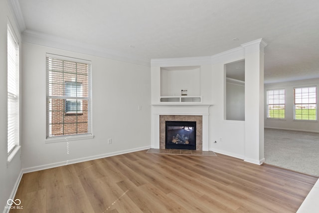 unfurnished living room with a tiled fireplace, ornamental molding, light wood finished floors, and baseboards