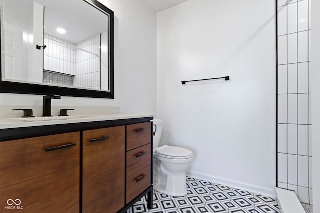 full bath featuring toilet, baseboards, tiled shower, and vanity