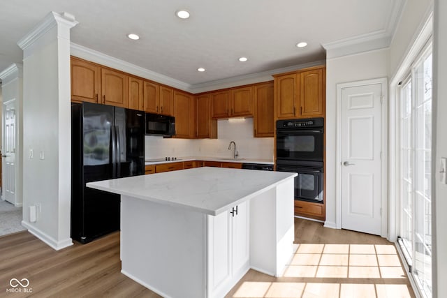 kitchen featuring crown molding, a center island, light wood-type flooring, a sink, and black appliances