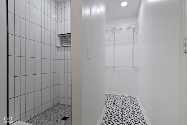 full bath featuring baseboards, a spacious closet, and tiled shower