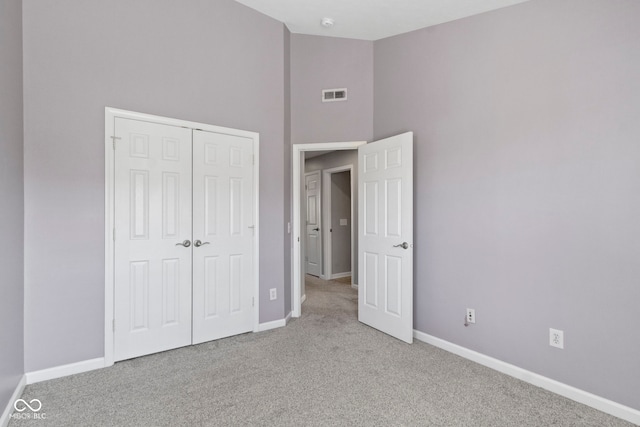 unfurnished bedroom featuring high vaulted ceiling, carpet, baseboards, visible vents, and a closet
