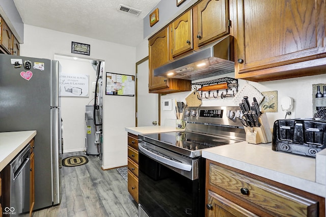 kitchen featuring visible vents, light wood-type flooring, under cabinet range hood, water heater, and stainless steel appliances