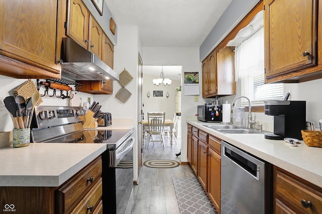 kitchen with wood finished floors, light countertops, under cabinet range hood, a sink, and appliances with stainless steel finishes