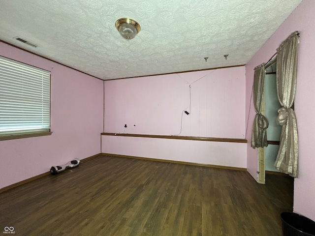 empty room with a textured ceiling, baseboards, wood finished floors, and visible vents