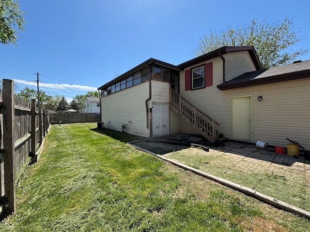 rear view of property with a fenced backyard, a yard, and stairway