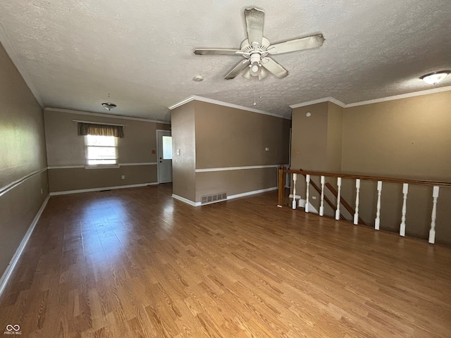 spare room featuring a ceiling fan, visible vents, ornamental molding, and wood finished floors
