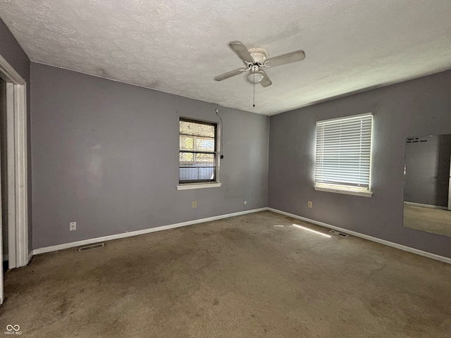 empty room with carpet flooring, ceiling fan, a textured ceiling, baseboards, and visible vents