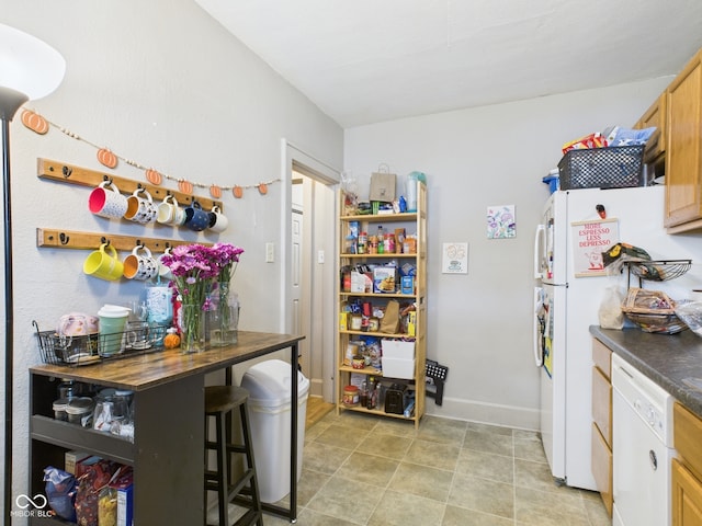 kitchen featuring dark countertops, baseboards, and white appliances
