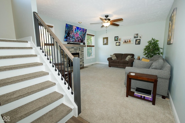 carpeted living area with ceiling fan, baseboards, stairway, and a fireplace