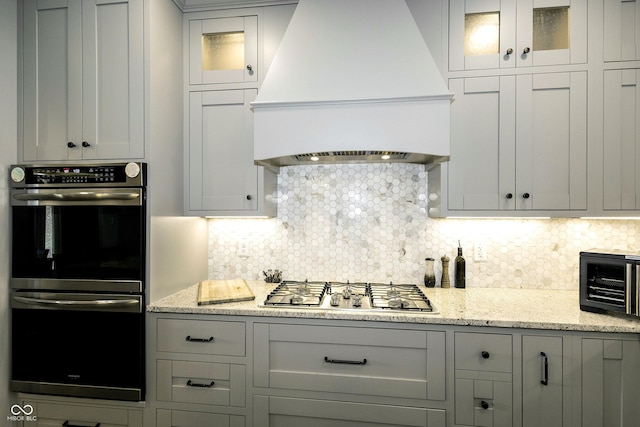 kitchen with gray cabinets, tasteful backsplash, custom exhaust hood, glass insert cabinets, and stainless steel appliances