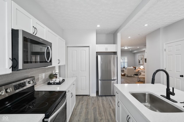 1417 E Michigan St, Indianapolis, IN 46201 - kitchen featuring white cabinets, appliances with stainless steel finishes, a sink, light wood-style floors, and a textured ceiling