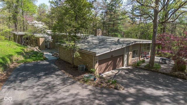 view of side of property with a shingled roof, an attached garage, central AC, a chimney, and driveway