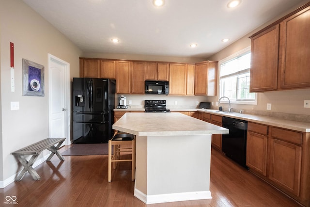 kitchen featuring wood finished floors, a kitchen island, light countertops, a sink, and black appliances