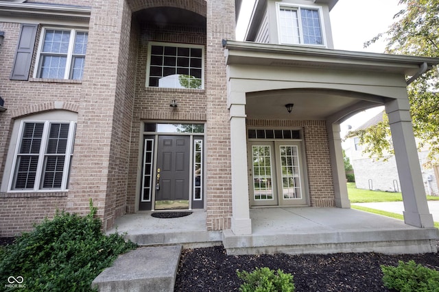 view of exterior entry featuring covered porch and brick siding