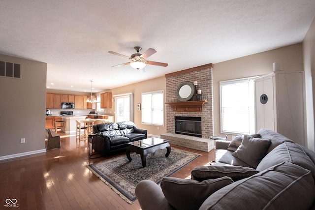 living area featuring visible vents, a brick fireplace, baseboards, dark wood-style floors, and a ceiling fan