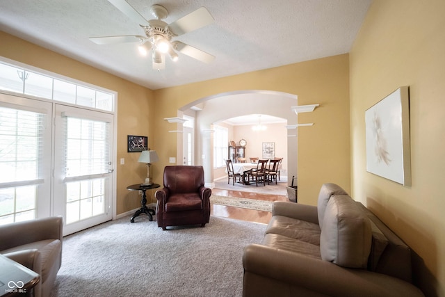 living room featuring arched walkways, ceiling fan, decorative columns, and plenty of natural light