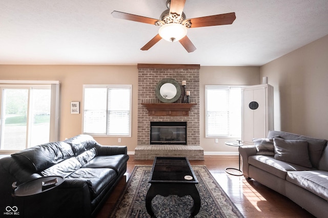 living room with baseboards, a ceiling fan, a brick fireplace, and wood finished floors