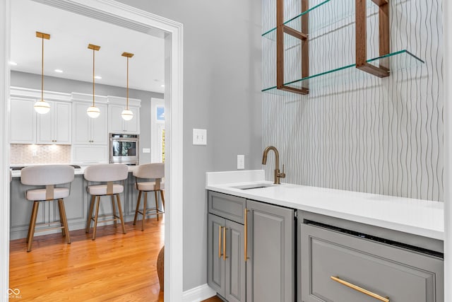 bar with decorative backsplash, stainless steel double oven, decorative light fixtures, light wood-type flooring, and a sink