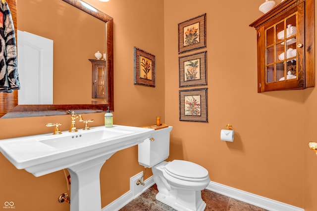 half bath featuring baseboards, a sink, tile patterned floors, and toilet