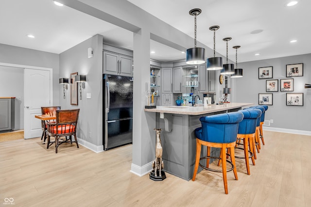 kitchen featuring open shelves, gray cabinets, light wood-style flooring, freestanding refrigerator, and baseboards