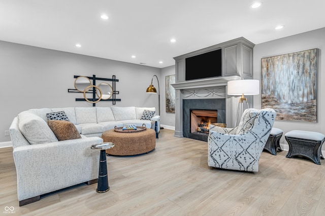 living room with recessed lighting, baseboards, a tiled fireplace, and light wood finished floors