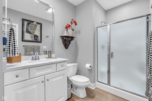 bathroom featuring wood finished floors, a stall shower, toilet, and vanity