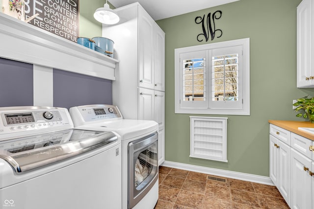 clothes washing area with visible vents, baseboards, independent washer and dryer, and cabinet space