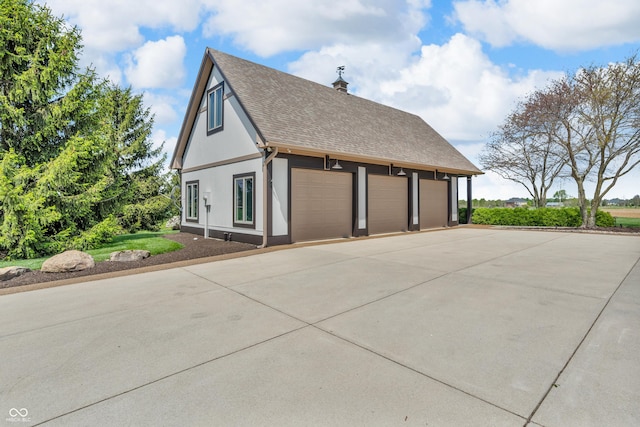view of side of property featuring roof with shingles, a detached garage, a chimney, and stucco siding
