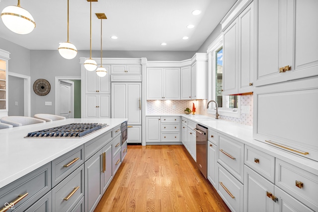 kitchen featuring appliances with stainless steel finishes, a sink, light wood finished floors, light countertops, and gray cabinetry