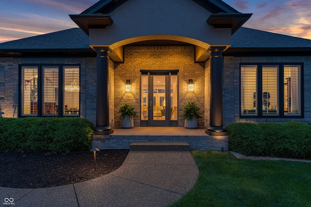 exterior entry at dusk featuring brick siding and a shingled roof